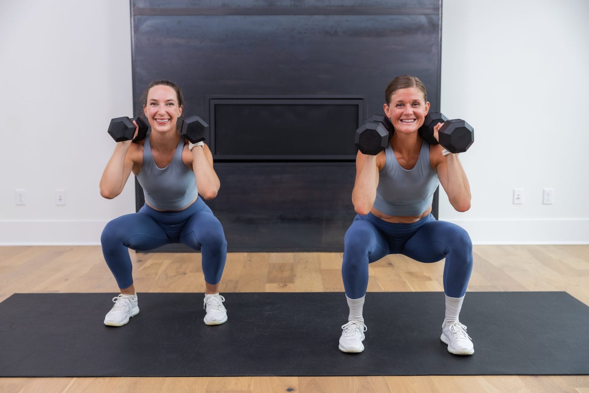 two women holding a low squat with dumbbells front racked in a thrusters workout